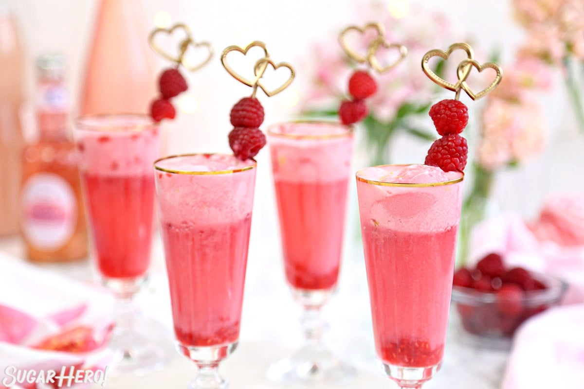 Four gold-rimmed champagne glasses filled with frothy pink Valentine's Day punch.
