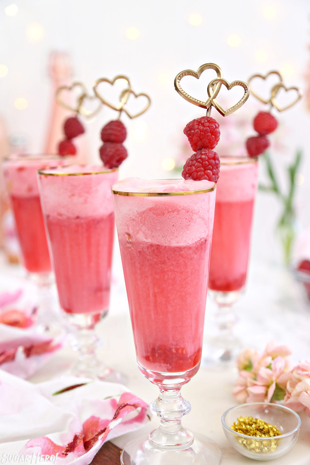 Tall gold-rimmed glasses with pink punch inside and a fresh raspberry garnish.
