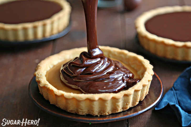 Chocolate ganache pouring into tart shell filled with caramel