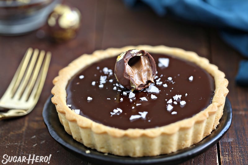 Baileys Chocolate Caramel Tart on a black plate with a chocolate truffle on top