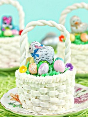 Close of up an Easter Basket Cupcake on a small round plate with floral design and two other Easter basket cupcakes in the background.
