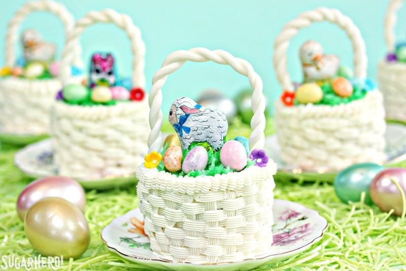 Five Easter basket cupcakes sitting on small round plates sitting on a bed of grass.