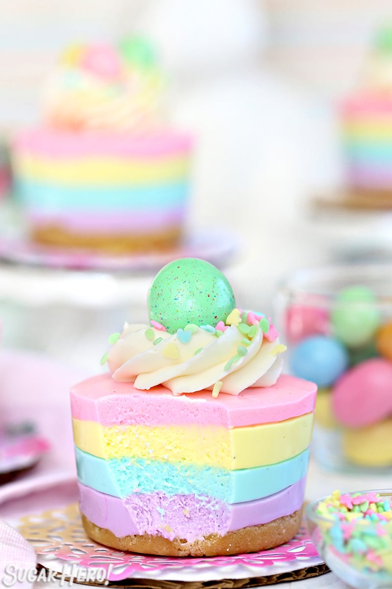 Easter No-Bake Mini Cheesecakes - pastel striped cheesecakes that are super easy, no baking required! | From SugarHero.com Easter no-bake mini cheesecake topped with frosting, sprinkles and a candy egg.