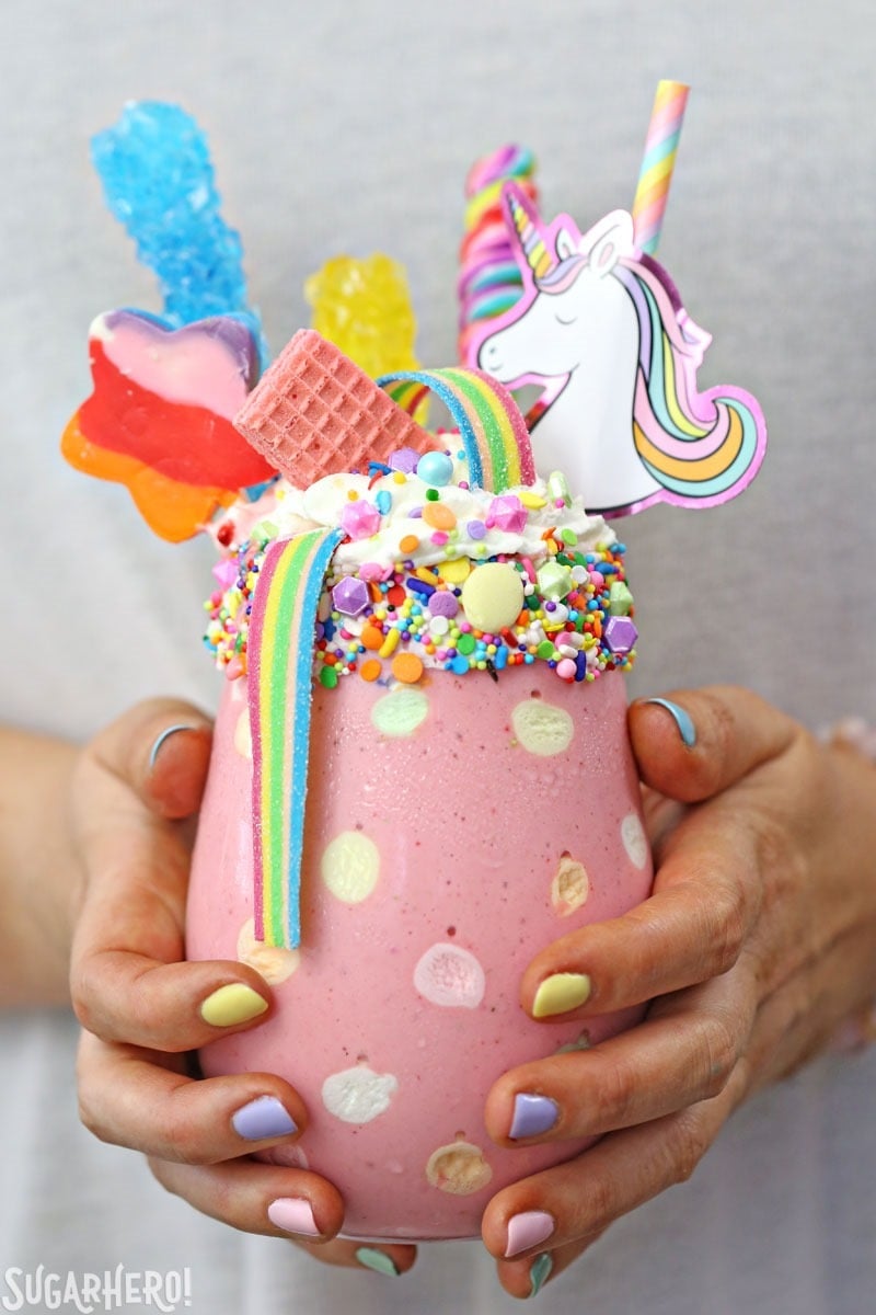 Unicorn Milkshakes - strawberry milkshakes in a polka-dot glass, topped with lots of rainbow candies. | From SugarHero.com