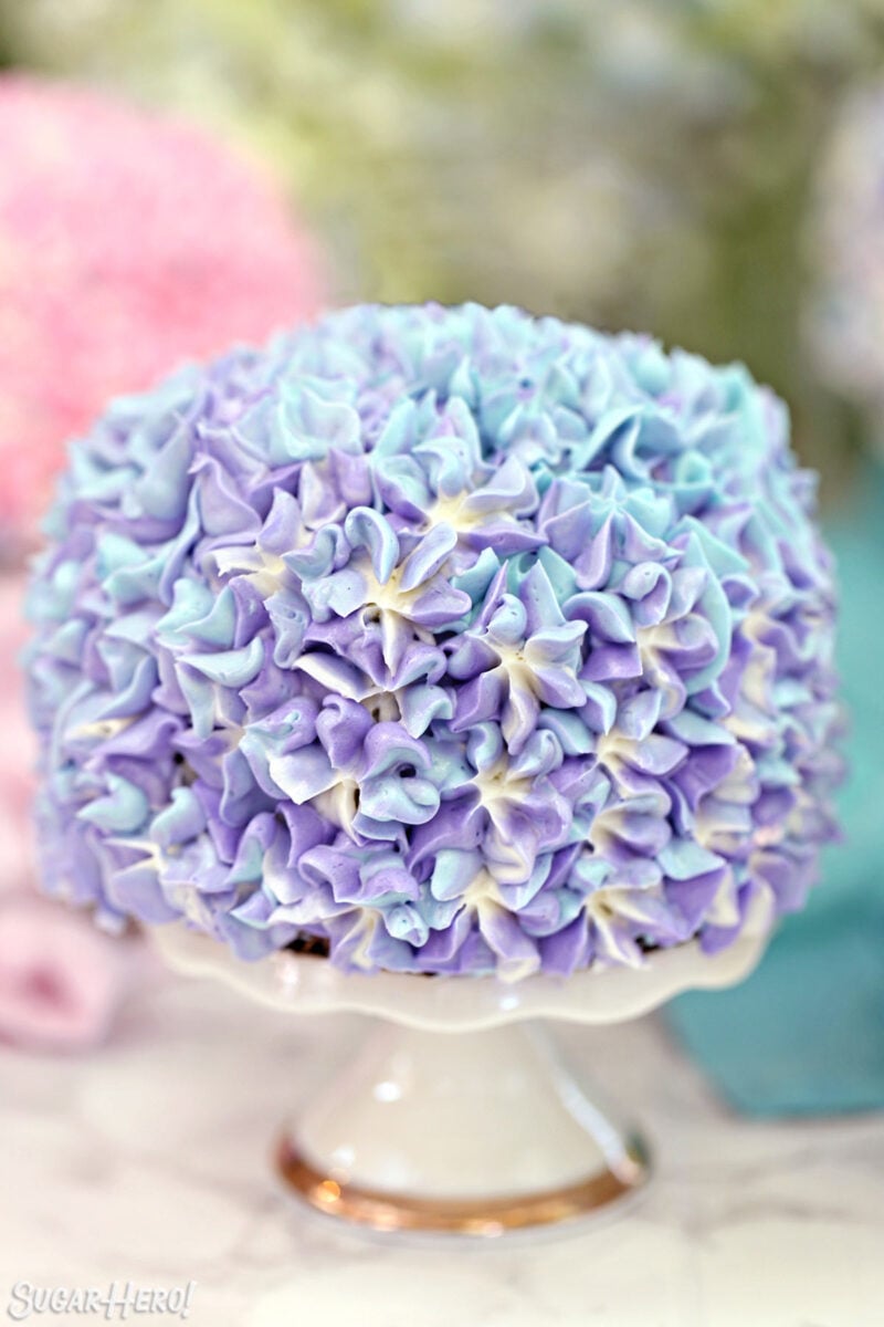 Close up of a purple hydrangea cake on a small white cake stand.