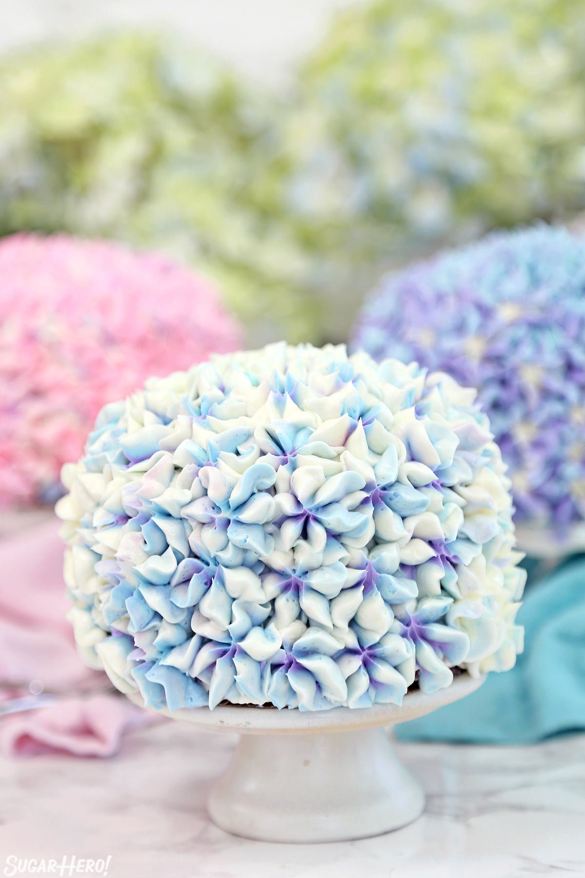 Three hydrangea cakes on small white cake stands.