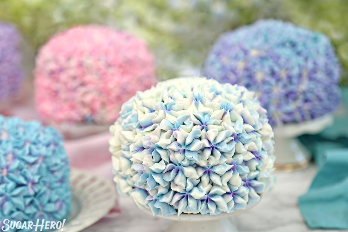 Hydrangea Cakes - A close up on one cake with others cakes blurred in the back, showing all the multi colored cakes. | From SugarHero.com