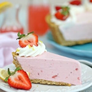 Slice of Strawberry Lemonade Ice Cream Pie on a white plate next to lemons and strawberries.