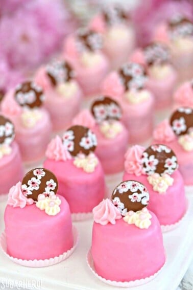 Rows of Cherry Blossom Petit Fours in small white candy cups on a white platter.