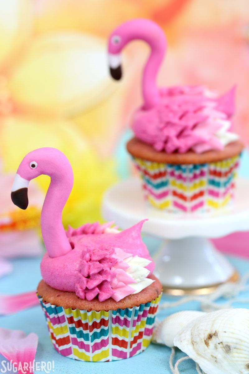 Flamingo Cupcakes - pink lemonade cupcakes decorated to look like pink flamingos! Easy, cute, and perfect for summer! Two Pink Lemonade Flamingo Cupcakes, one on a cupcake stand