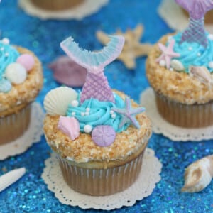 Close up of Mermaid Cupcakes on white doilies and blue glitter.