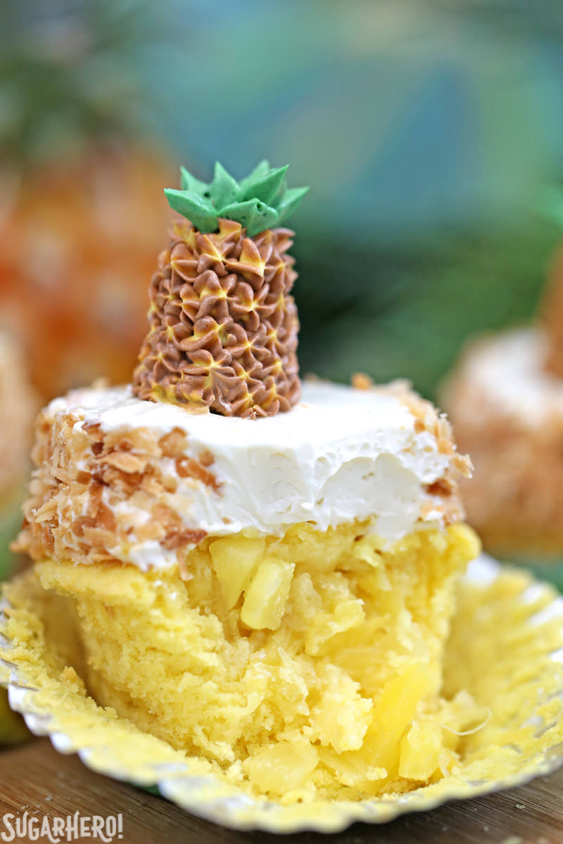 Pineapple cupcake with a bite taken out of it and fresh pineapple in the middle, topped with coconut buttercream | From SugarHero.com