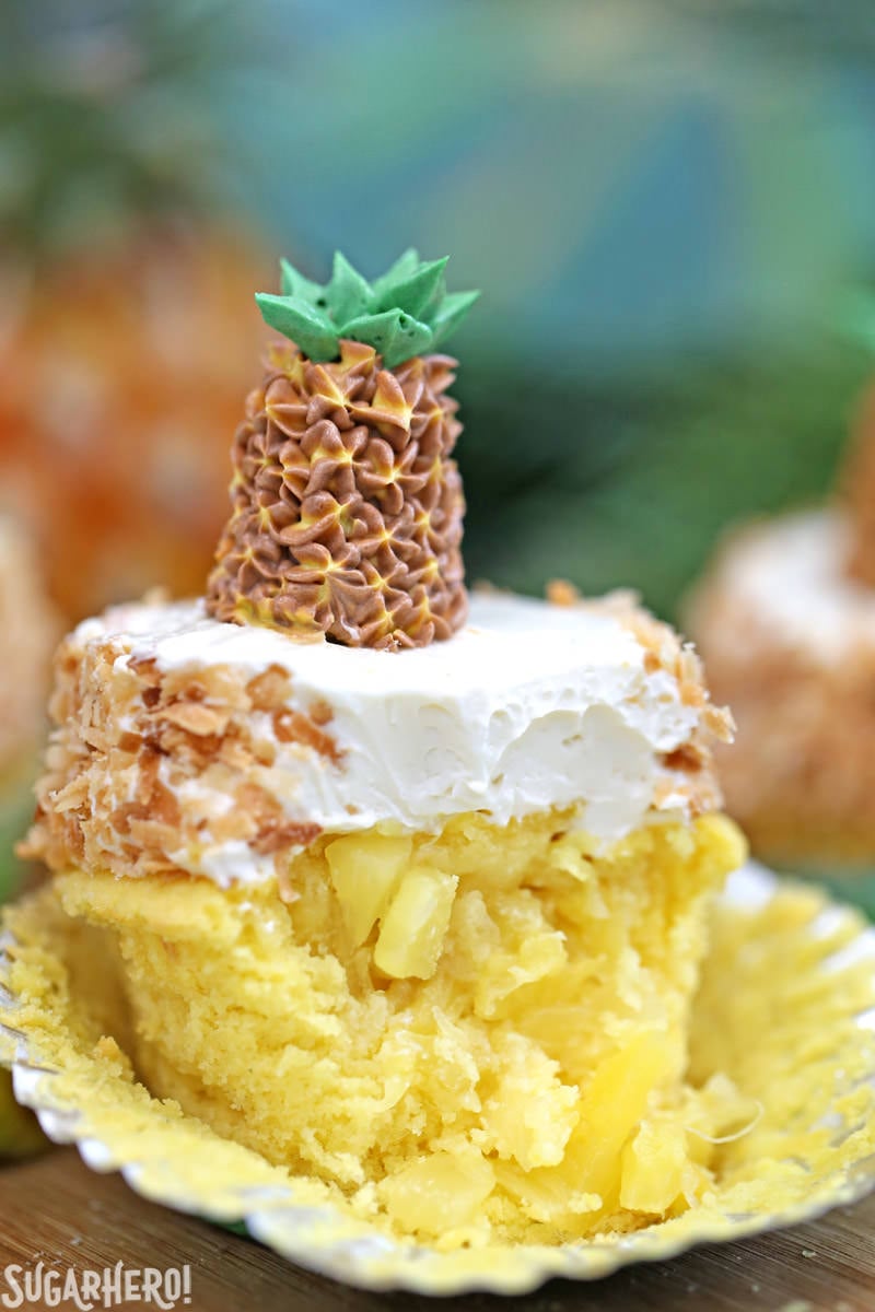 Pineapple Cupcakes - fun and tropical pineapple cupcakes with coconut frosting. Plus an adorable buttercream pineapple on top! | From SugarHero.com Pineapple cupcake with a bite taken out of it and fresh pineapple in the middle, topped with coconut buttercream | From SugarHero.com