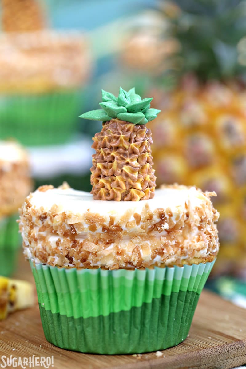 Pineapple Cupcakes - fun and tropical pineapple cupcakes with coconut frosting. Plus an adorable buttercream pineapple on top! | From SugarHero.com Close-up of a single pineapple cupcake with coconut frosting and a buttercream pineapple on top | From SugarHero.com