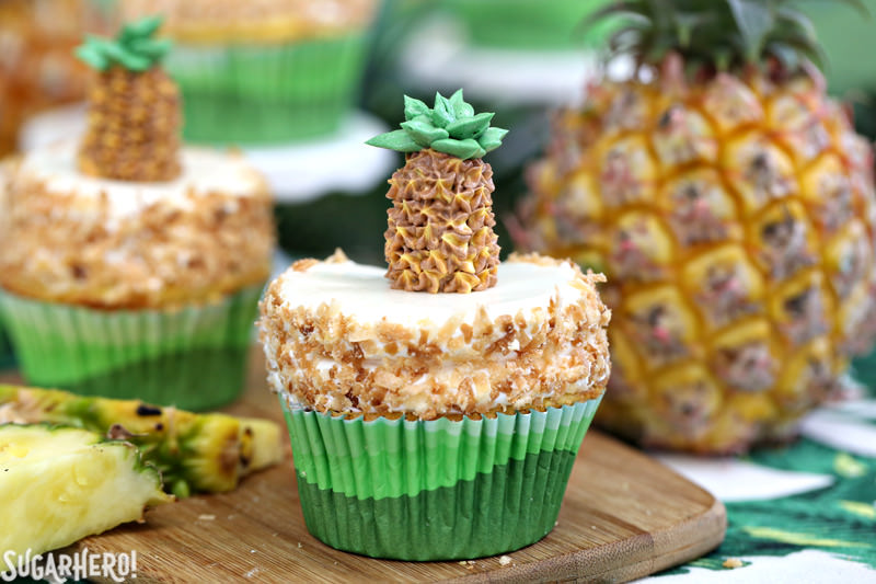 Two pineapple cupcakes with coconut buttercream and fresh pineapple pieces | From SugarHero.com