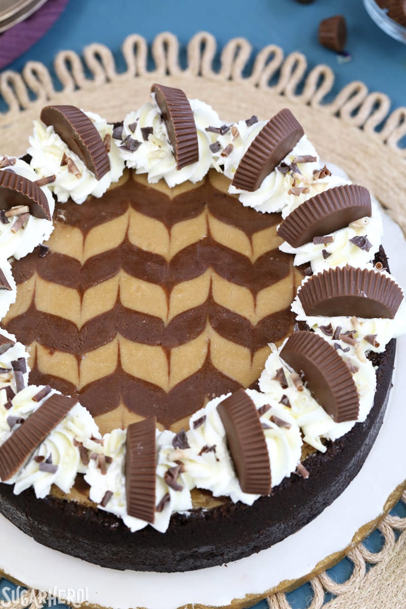 Chocolate Peanut Butter Cheesecake - this is the ULTIMATE cheesecake! Smooth and creamy, with gorgeous chocolate swirls and lots of peanut butter cups! | From SugarHero.com Chocolate Peanut Butter Cheesecake with whipped cream and peanut butter cups on top | From SugarHero.com