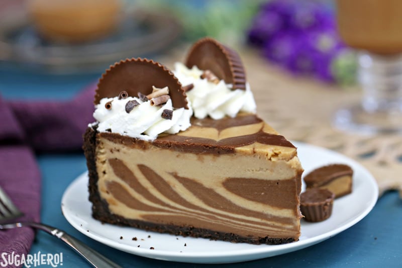 Chocolate Peanut Butter Cheesecake - this is the ULTIMATE cheesecake! Smooth and creamy, with gorgeous chocolate swirls and lots of peanut butter cups! | From SugarHero.com Chocolate Peanut Butter Cheesecake slice, with whipped cream and peanut butter cups on top | From SugarHero.com