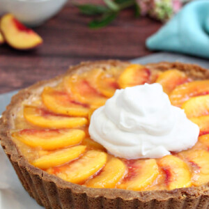Close up of a Fresh Peach Tart with a large dollop of whipped cream on top.