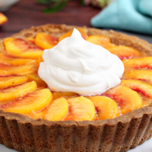 Close up of a Fresh Peach Tart with a large dollop of whipped cream on top.