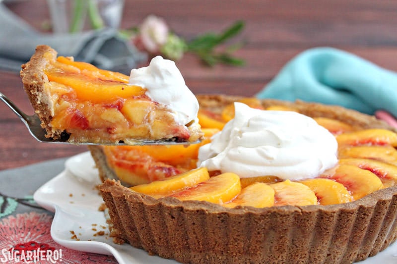Lifting out a slice of Fresh Peach Tart, a no-bake tart recipe featuring juicy ripe peaches in a buttery shell | From SugarHero.com