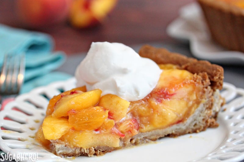 Fresh Peach Tart - the BEST way to enjoy peaches! No-bake tart recipe featuring juicy ripe peaches in a buttery shell | From SugarHero.com A close-up on a slice of no-bake Fresh Peach Tart, topped with whipped cream | From SugarHero.com