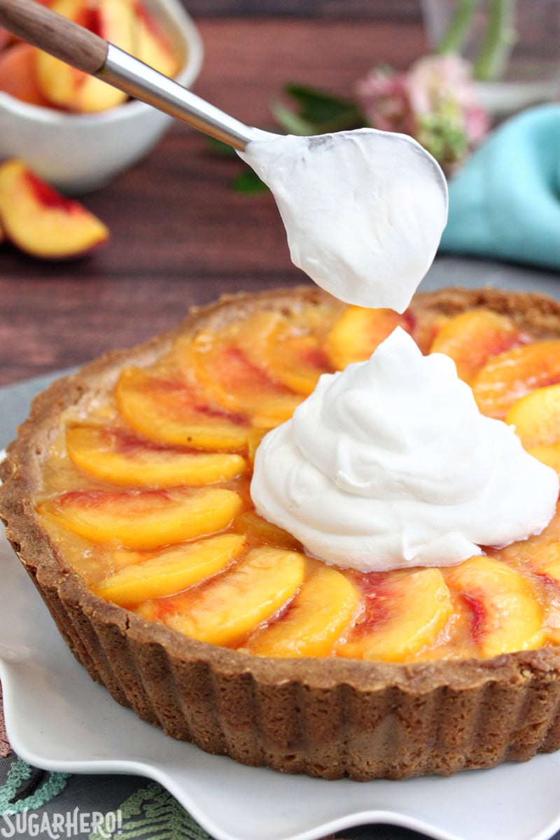 Fresh Peach Tart - the BEST way to enjoy peaches! No-bake tart recipe featuring juicy ripe peaches in a buttery shell | From SugarHero.com Putting a dollop of whipped cream on a no-bake Fresh Peach Tart | From SugarHero.com