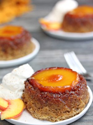 Single Peach Upside-Down Cake on a white plate next to whipped cream and peach slices.