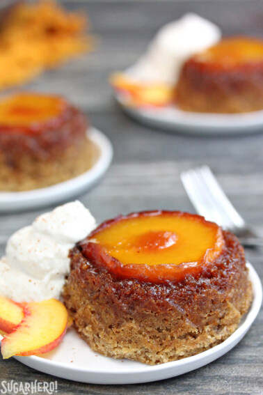Single Peach Upside-Down Cake on a white plate next to whipped cream and peach slices.