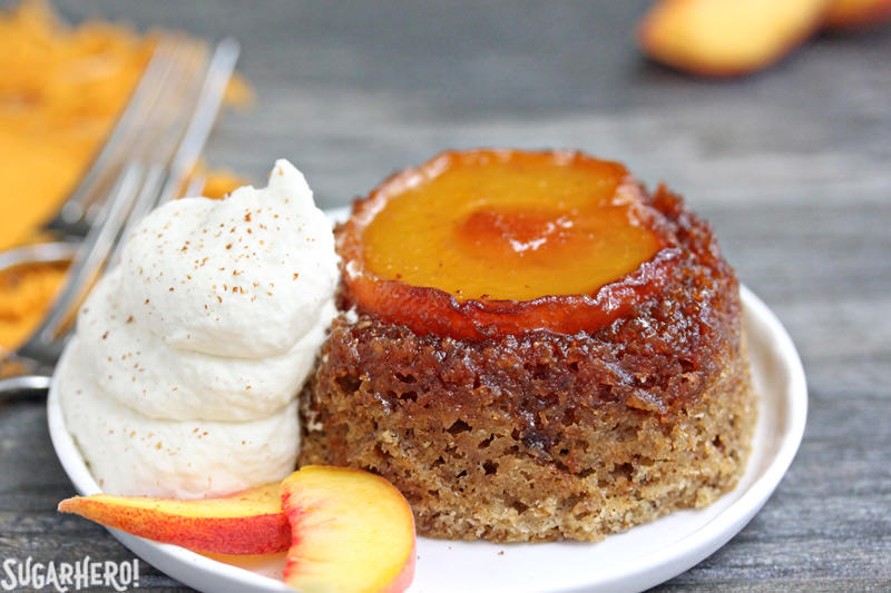Close-up of Peach Upside-Down Cakes on a plate with whipped cream and fresh peach slices | From SugarHero.com