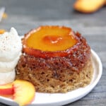 Single Peach Upside-Down Cake on a white plate next to whipped cream and peach slices.