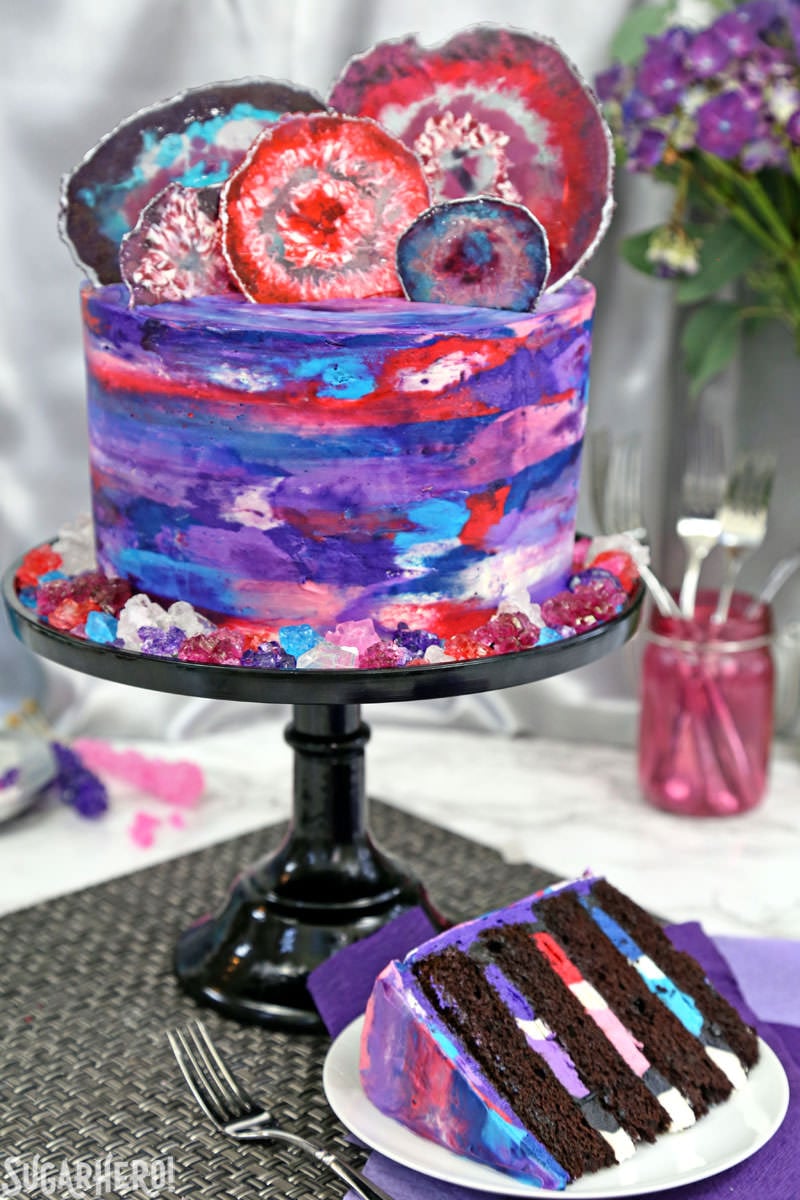 Agate Cake - with gorgeous, EDIBLE candy agate slices, and a pretty watercolor buttercream effect! | From SugarHero.com Agate Cake - chocolate cake with watercolor buttercream and candy agate slices on top, with a slice taken out | From SugarHero.com