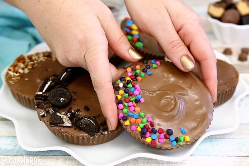 Mega Stuffed Peanut Butter Cups - jumbo homemade peanut butter cups, filled with goodies like candy, cookies, pretzels, or potato chips! | From SugarHero.com Mega Stuffed Peanut Butter Cups - hands holding a giant peanut butter cup topped with rainbow chips | From SugarHero.com