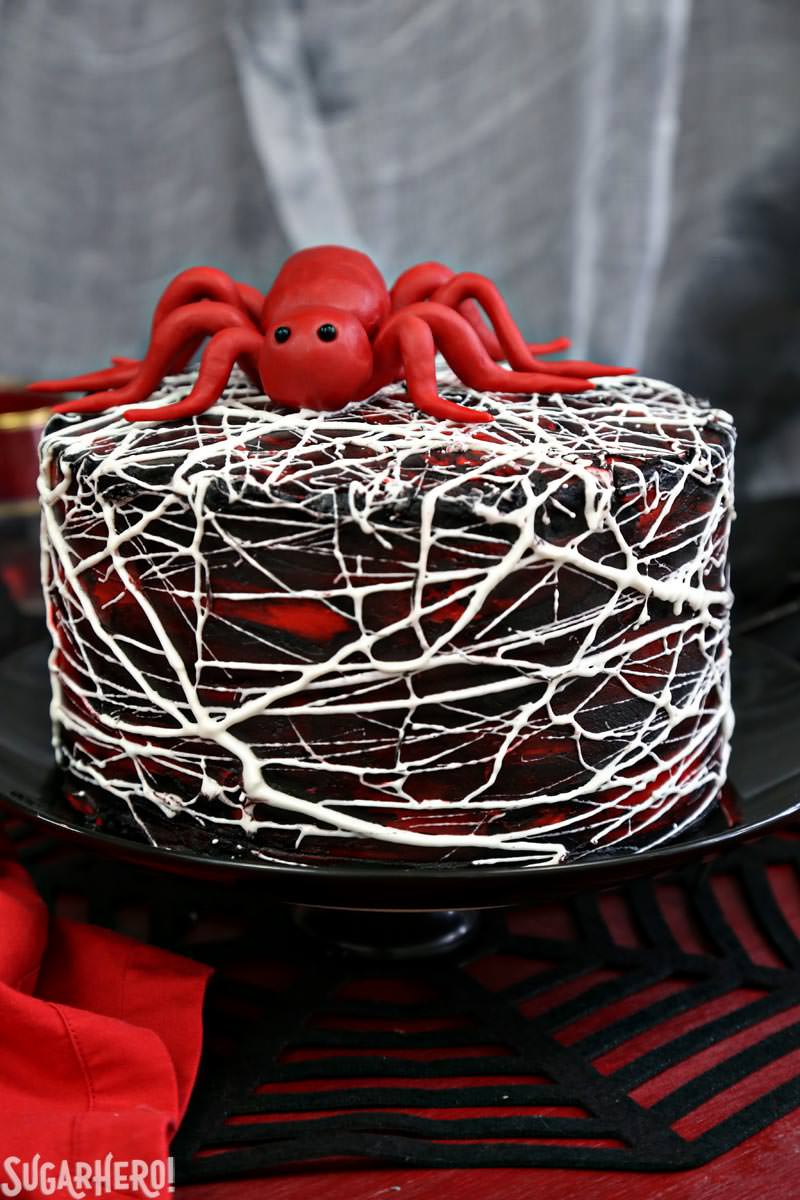 Red Velvet Marshmallow Spiderweb Cake—classic red velvet cake with black chocolate buttercream, covered with a web of marshmallow spiderwebs! | From SugarHero.com Red Velvet Marshmallow Spiderweb Cake with red candy spider on top | From SugarHero.com