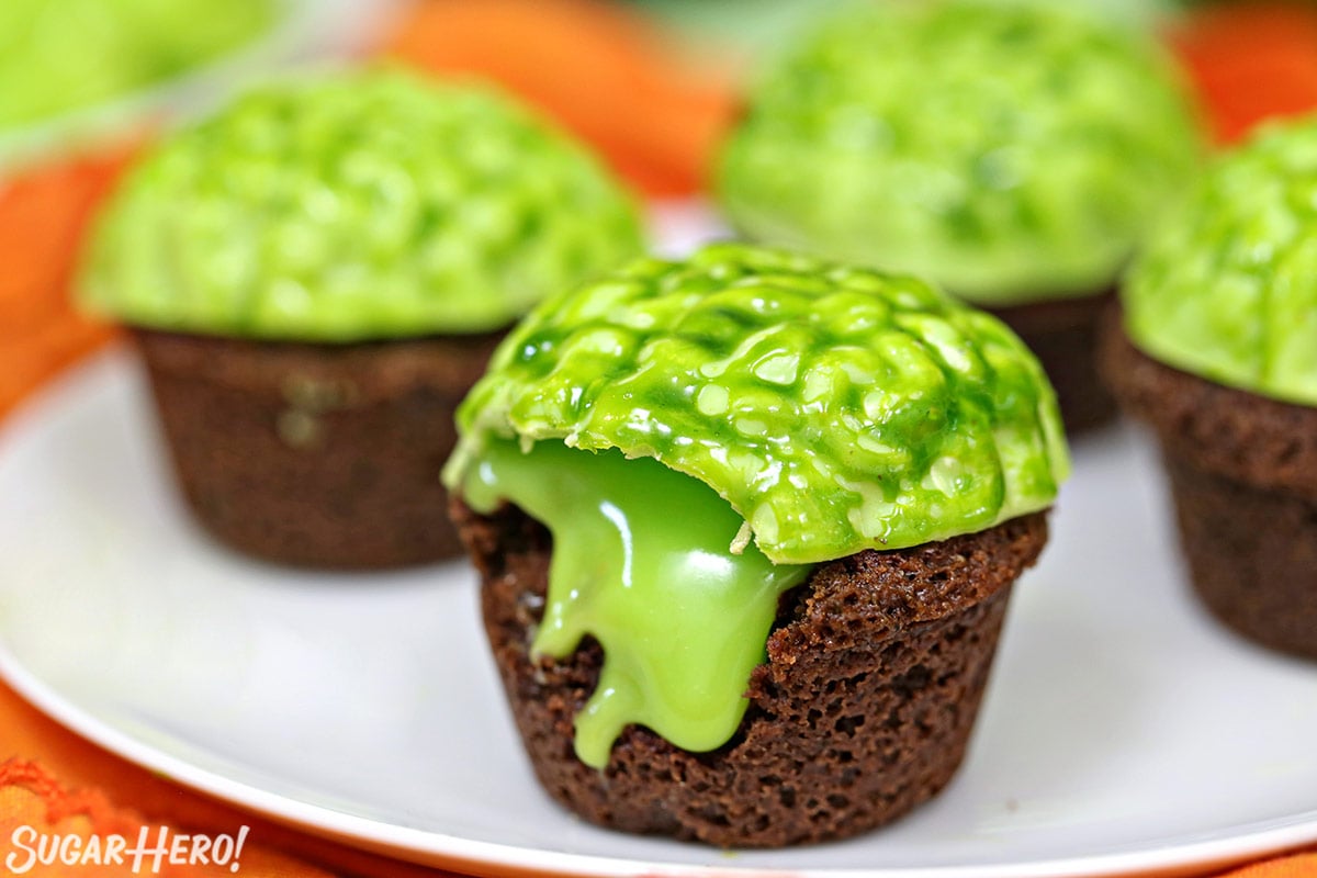 Zombie Brownie Bites - displayed on a cake stand, with a bite taken out of one | From SugarHero.com