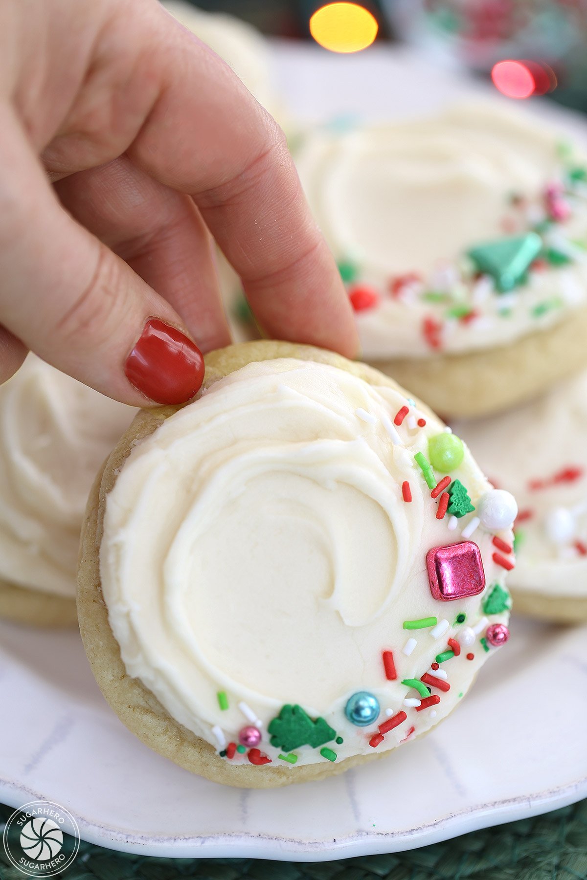 Hand with red fingernails lifting a Big Soft Sugar Cookie up from a plate of cookies.