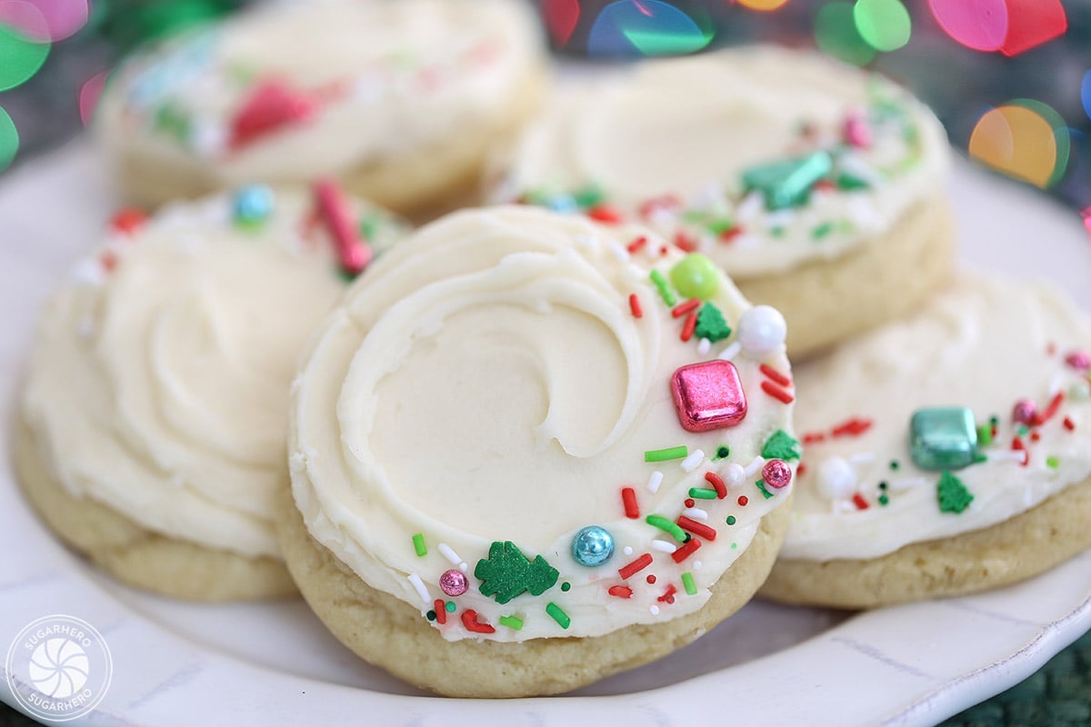 Frosted sugar cookies on a plate with colorful sprinkles.