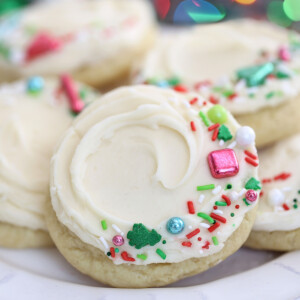 Plate of frosted sugar cookies with Christmas lights in the background.