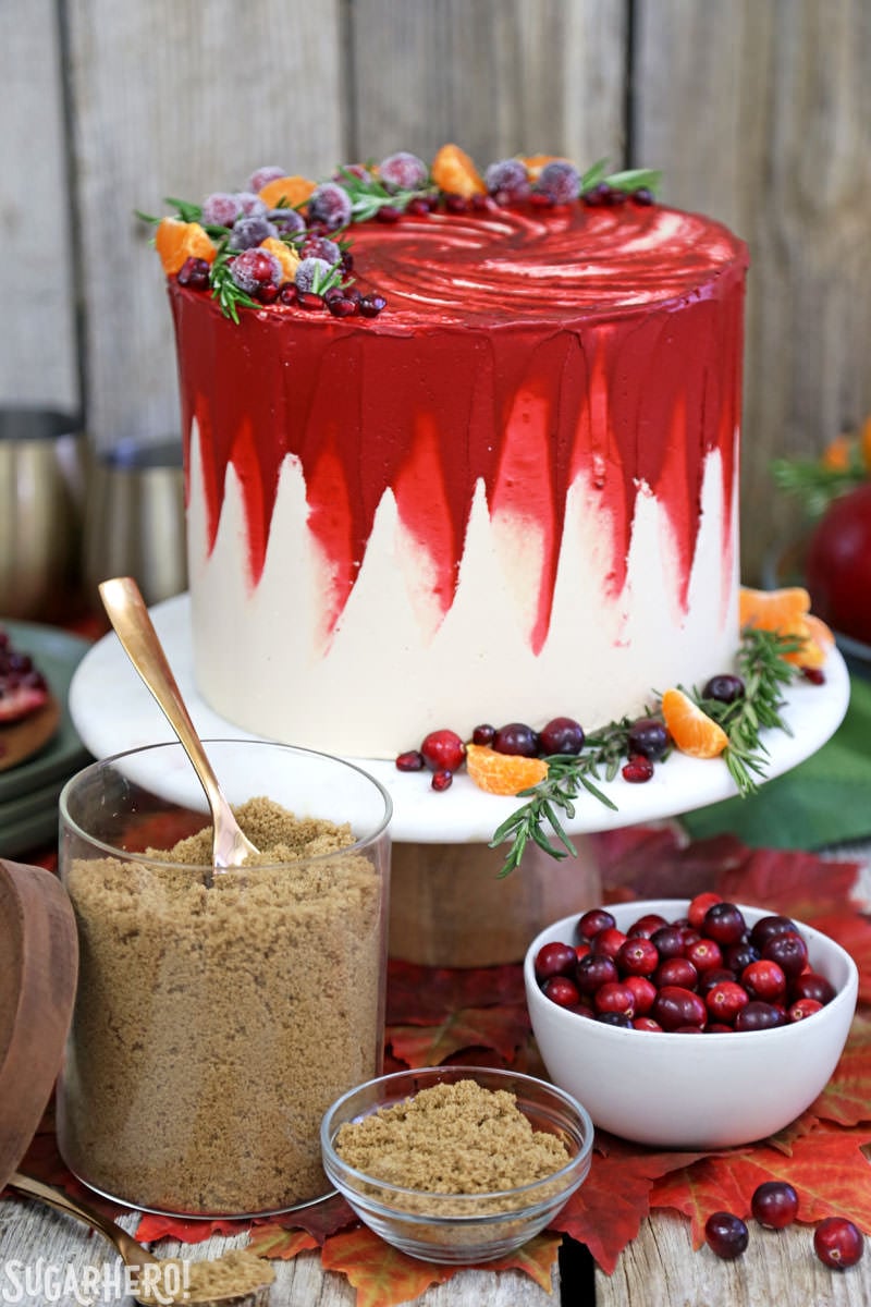 Brown Sugar Cranberry Cake - brown sugar spice cake, cranberry filling, and the MOST DELICIOUS brown sugar Swiss meringue buttercream! | From SugarHero.com Brown Sugar Cranberry Cake - cake with brown sugar and a bowl of cranberries in front | From SugarHero.com