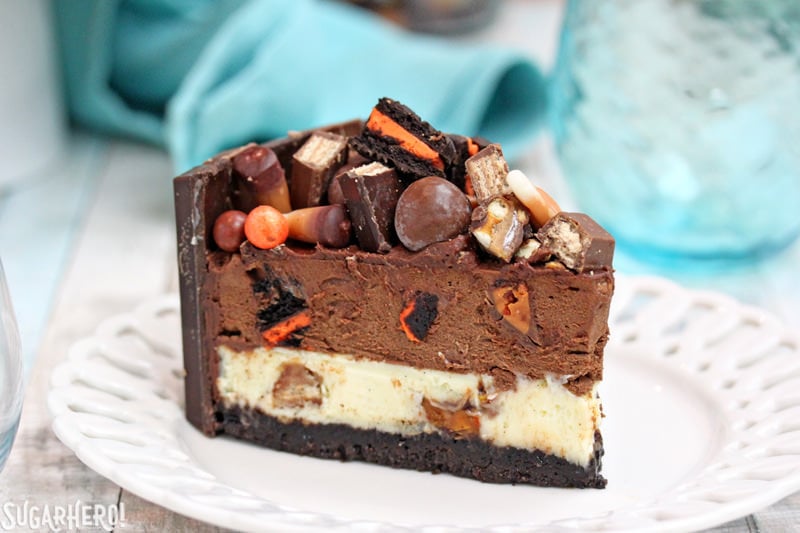 Candy Bar Cheesecake – a creamy chocolate-vanilla cheesecake PACKED with candy bars! It’s a great way to use up extra candy! | From SugarHero.com Candy Bar Cheesecake – single slice of candy bar cheesecake with candy on top | From SugarHero.com