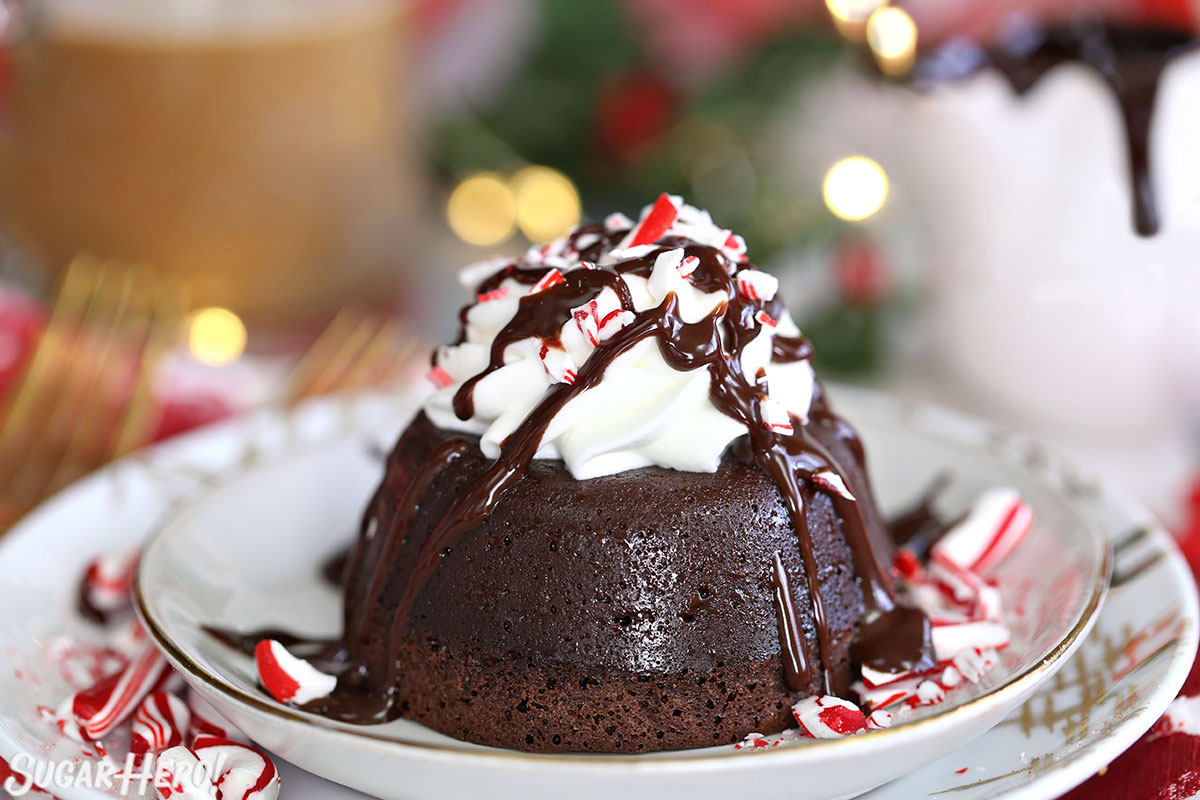 Peppermint Mocha Lava Cakes - close-up one one lava cake with coffee and chocolate sauce in the background | From SugarHero.com
