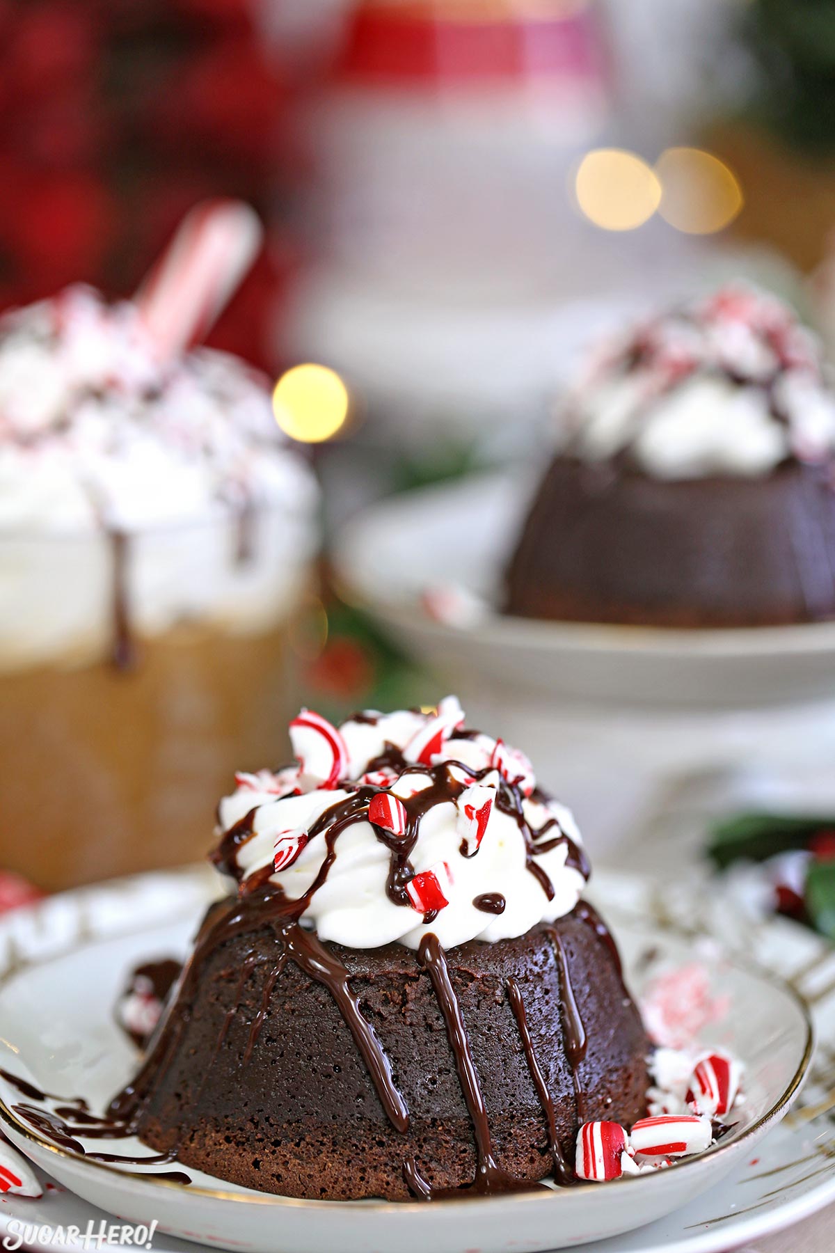 Peppermint Mocha Lava Cakes - two chocolate cakes topped with whipped cream, chocolate sauce, and candy canes, with coffee in the background | From SugarHero.com