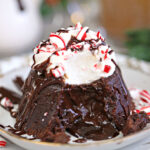 Close-up of Peppermint Lava Cake with whipped cream, chocolate drizzle, and candy cane pieces on top.