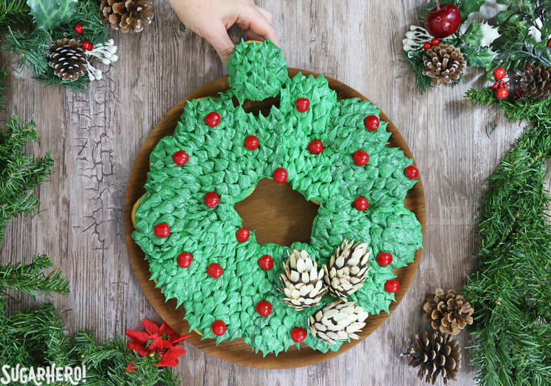 Pull-Apart Cupcake Wreath Cake - picture of hand removing a cupcake from the cupcake wreath. | From SugarHero.com