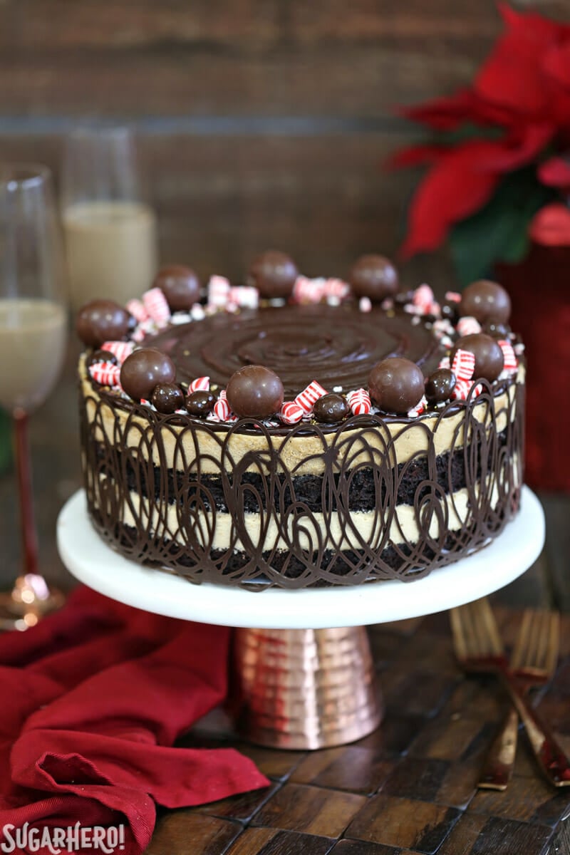 Peppermint Mocha Mousse Cake is the perfect holiday party cake! It features layers of brownies and peppermint mocha mousse, wrapped in chocolate swirls and topped with a shiny chocolate glaze. | From SugarHero.com Peppermint Mocha Mousse Cake - close-up of peppermint mocha mousse cake on cake stand | From SugarHero.com