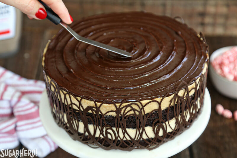 Peppermint Mocha Mousse Cake - smoothing a shiny chocolate glaze in a spiral pattern on top of the mousse cake | From SugarHero.com