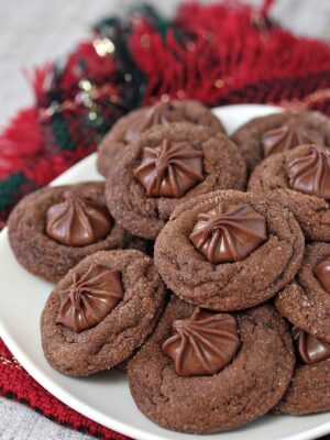 About a dozen soft chocolate gingerbread cookies on a white plate with a red and green napkin in the background.