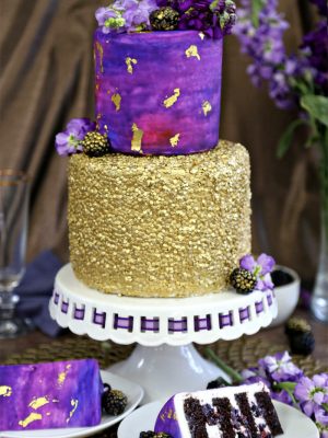 Close up of a Gold Sequin Watercolor Cake wit 2 slices on white plates in front.