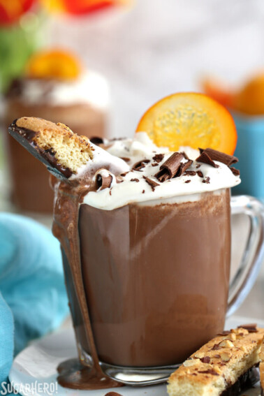 Orange Hot Chocolate with a biscotti inserted and cocoa drizzling down the side of the mug.