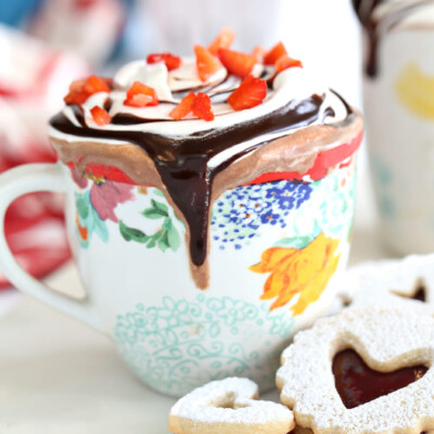 Strawberry hot chocolate in a floral mug with whipped cream and sliced strawberries on top.