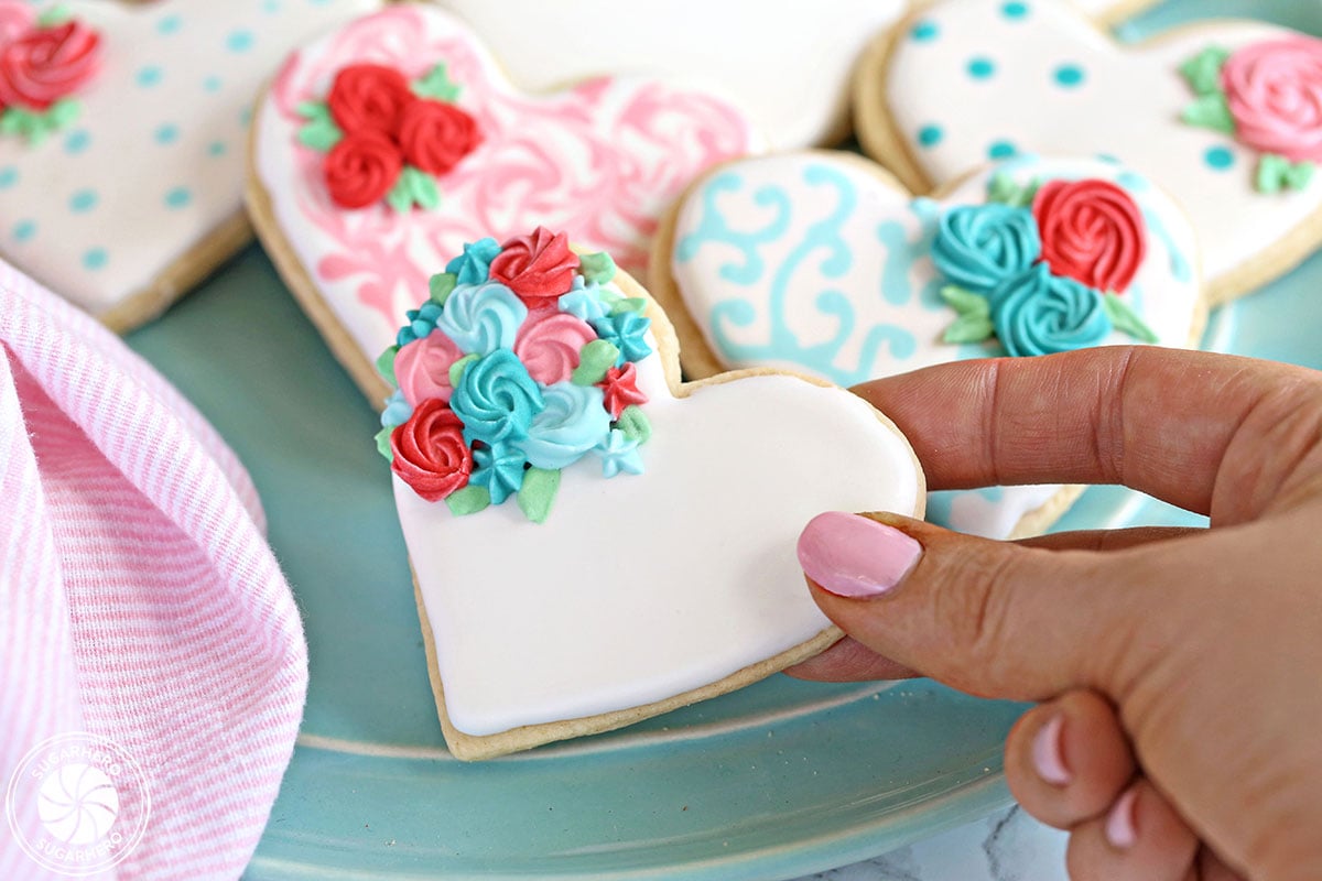 Valentine's Day Sugar Cookies - close-up of hand holding a sugar cookie decorated with royal icing for Valentine's Day | From SugarHero.com